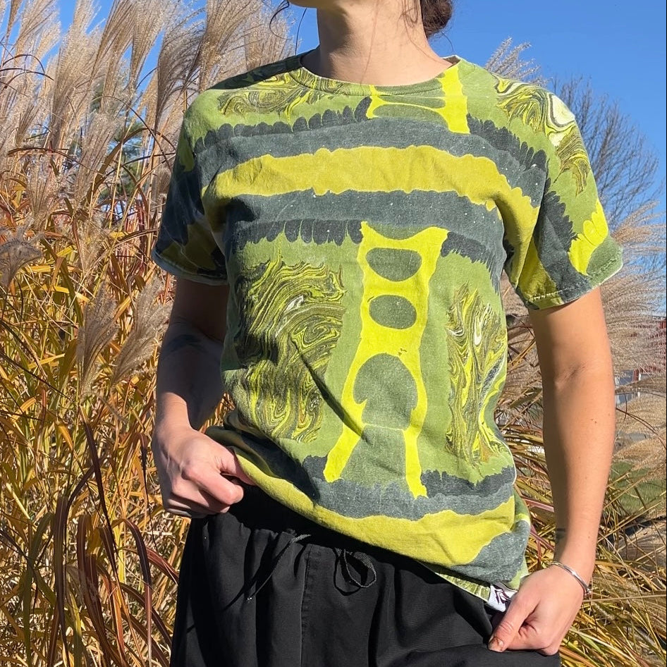 Person wearing a green and yellow patterned shirt standing in tall grass with a blue sky.